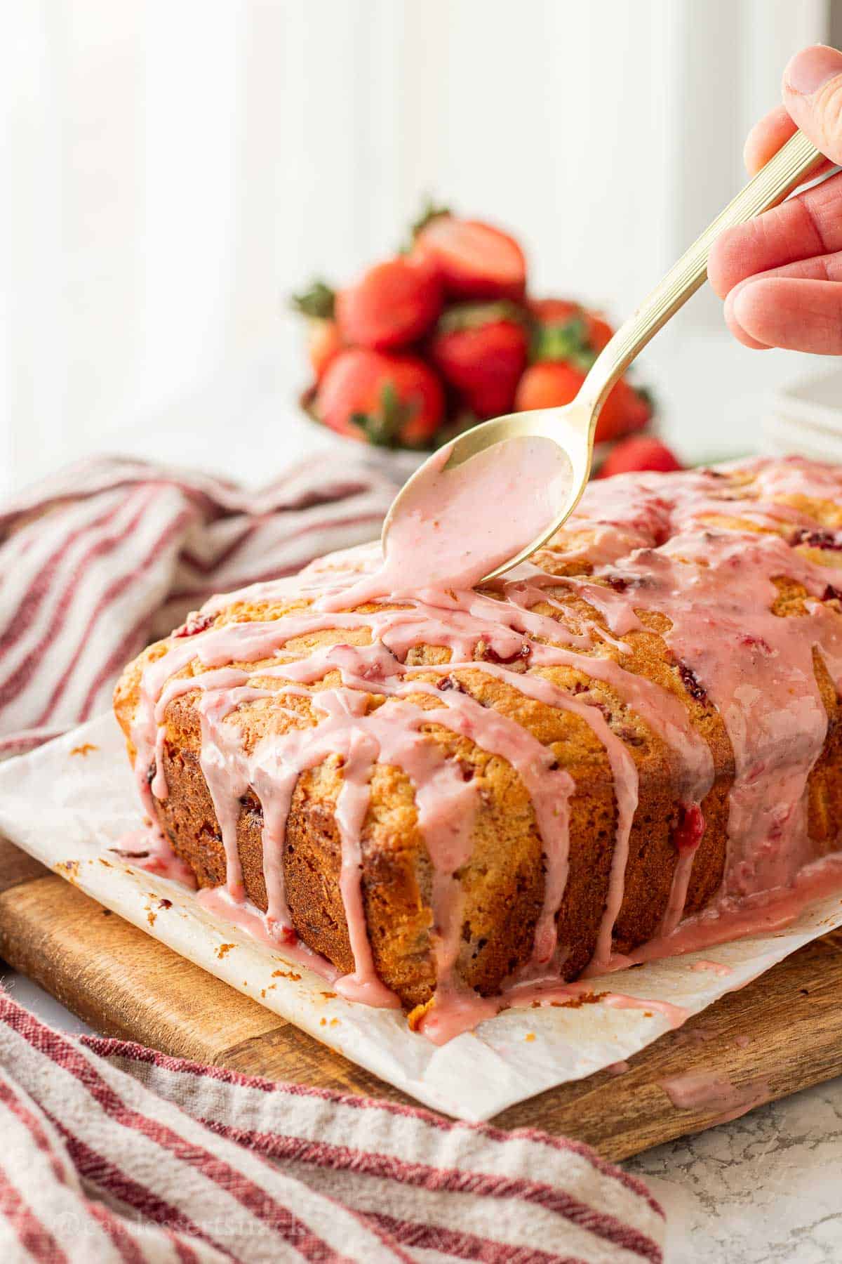Gold spoon with strawberry icing on baked banana strawberry bread loaf.