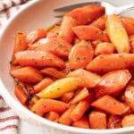 Cooked glazed carrots in white bowl.
