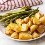Baked green beans and potatoes on white plate.