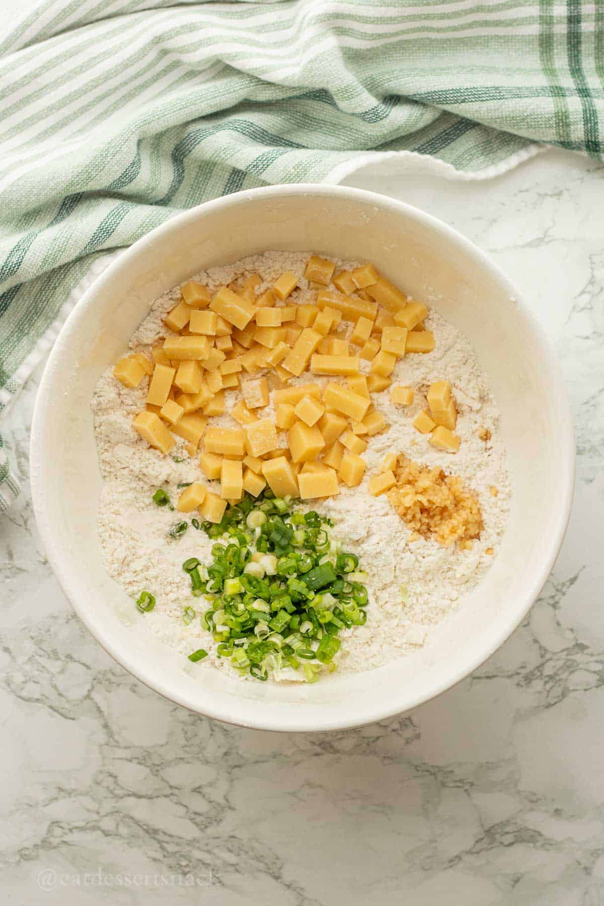 Cheese, garlic, and green onion in flour in white bowl.