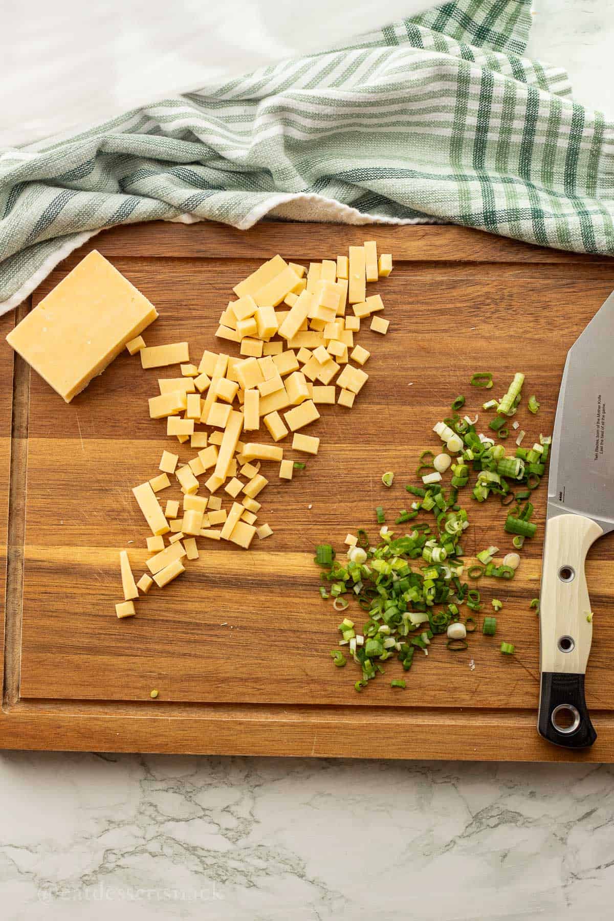Chopped cheese and green onion on wood cutting board.