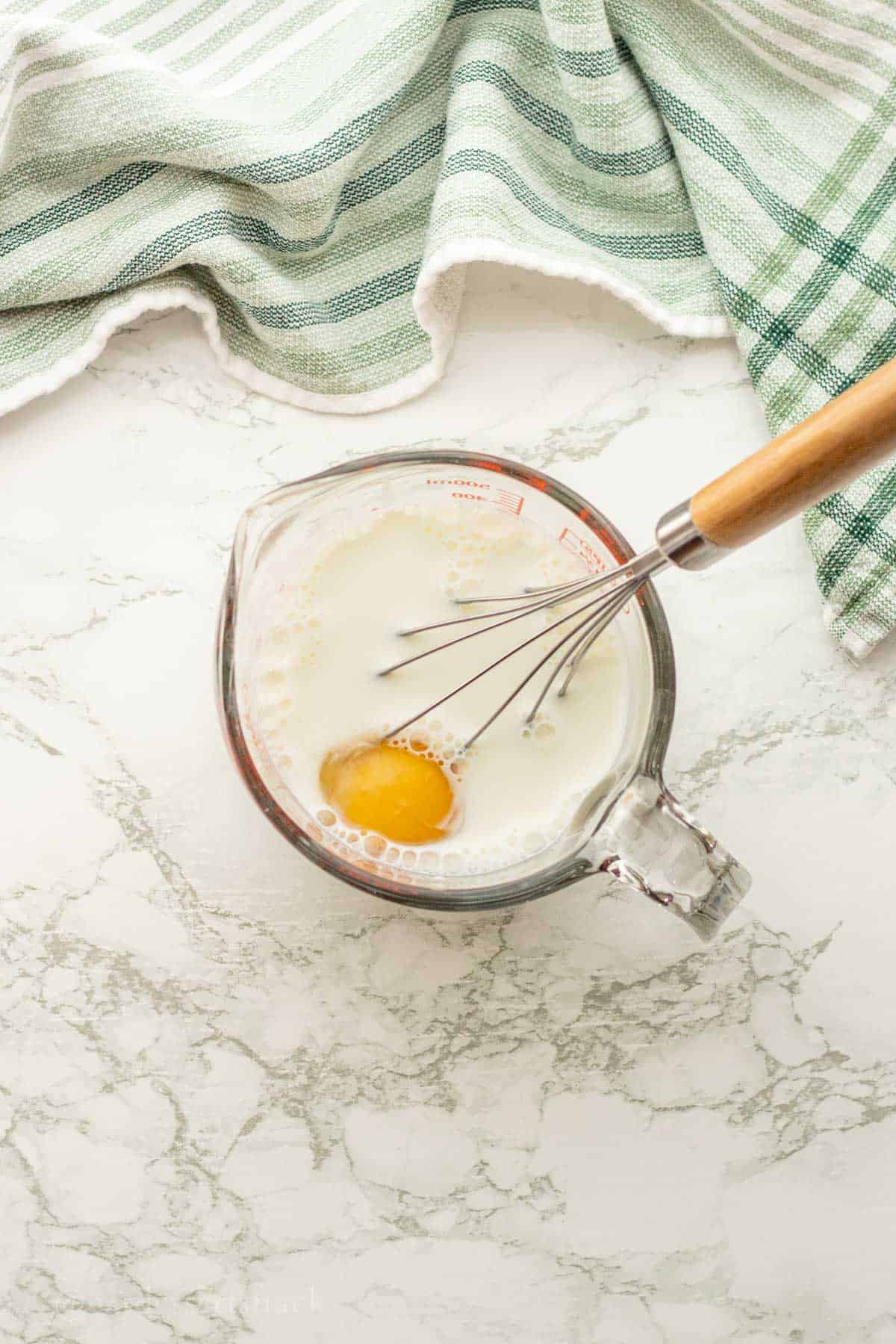 Egg in cup of milk with whisk.