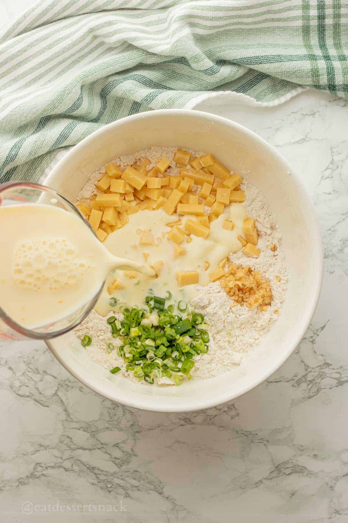 Pouring milk into dry ingredients in white bowl.