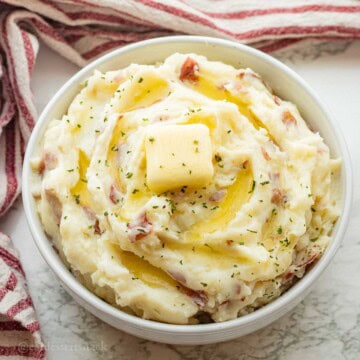Red skin mashed potatoes with butter on top in white bowl.
