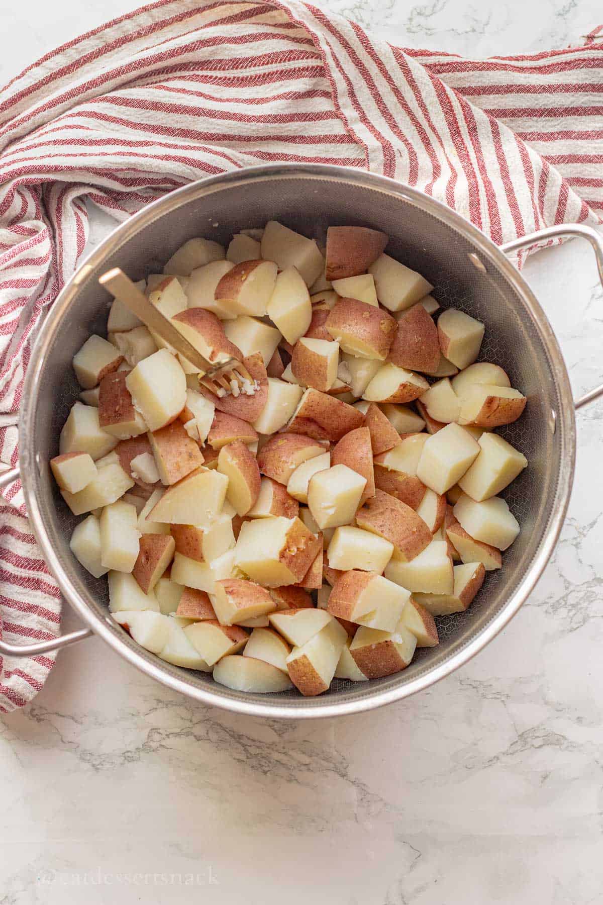 Cooked red potatoes with fork in metal pot.