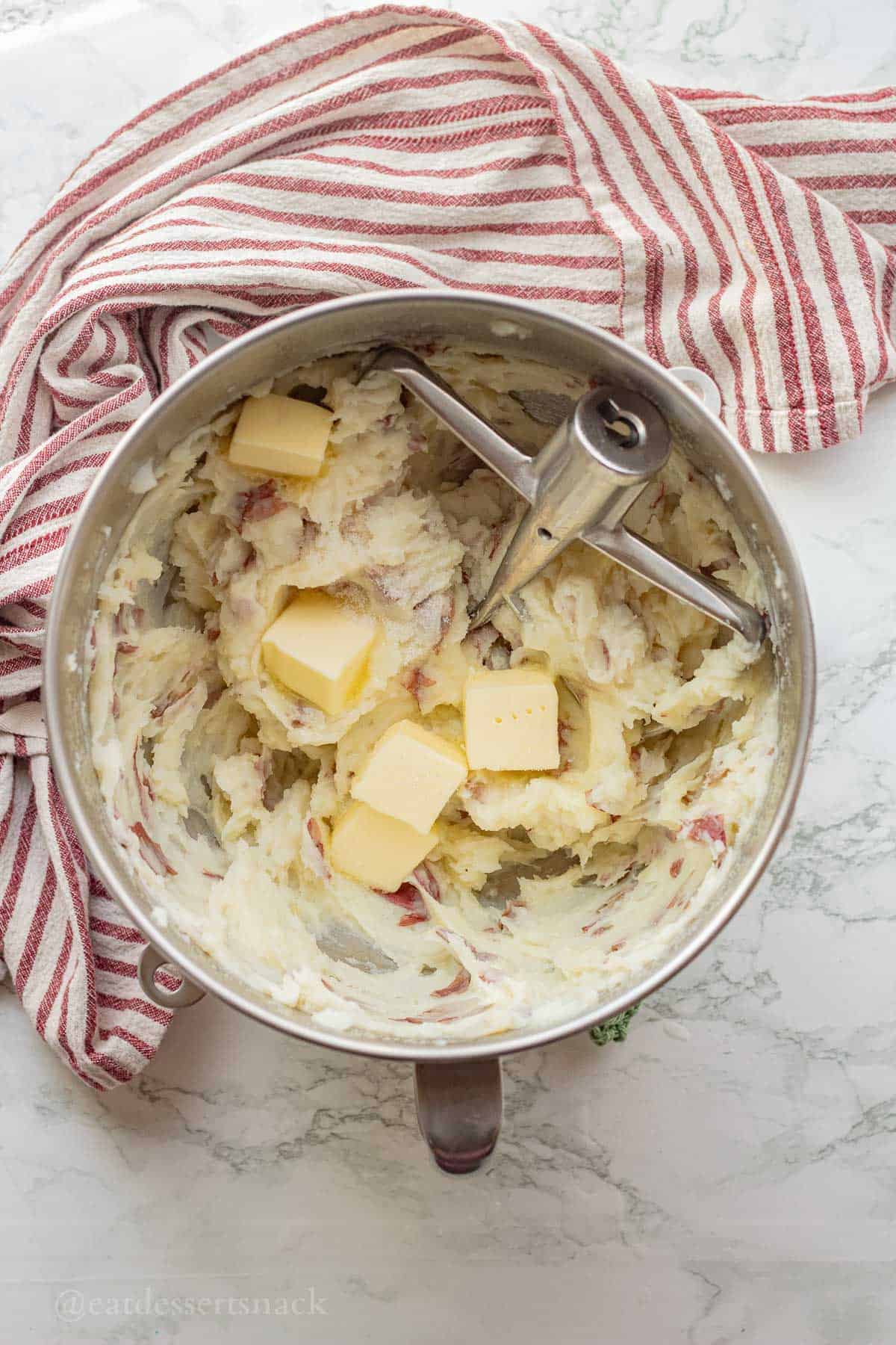 Butter in mixing bowl with potatoes and paddle attachment.