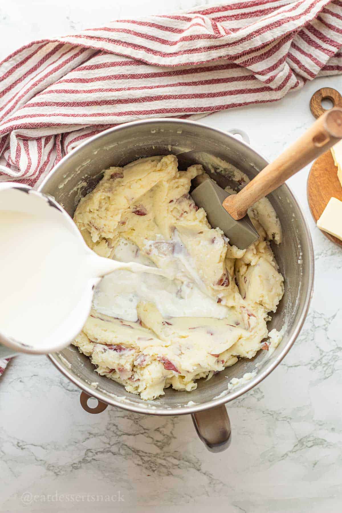 Pouring milk into mixing bowl of mashed red potatoes.