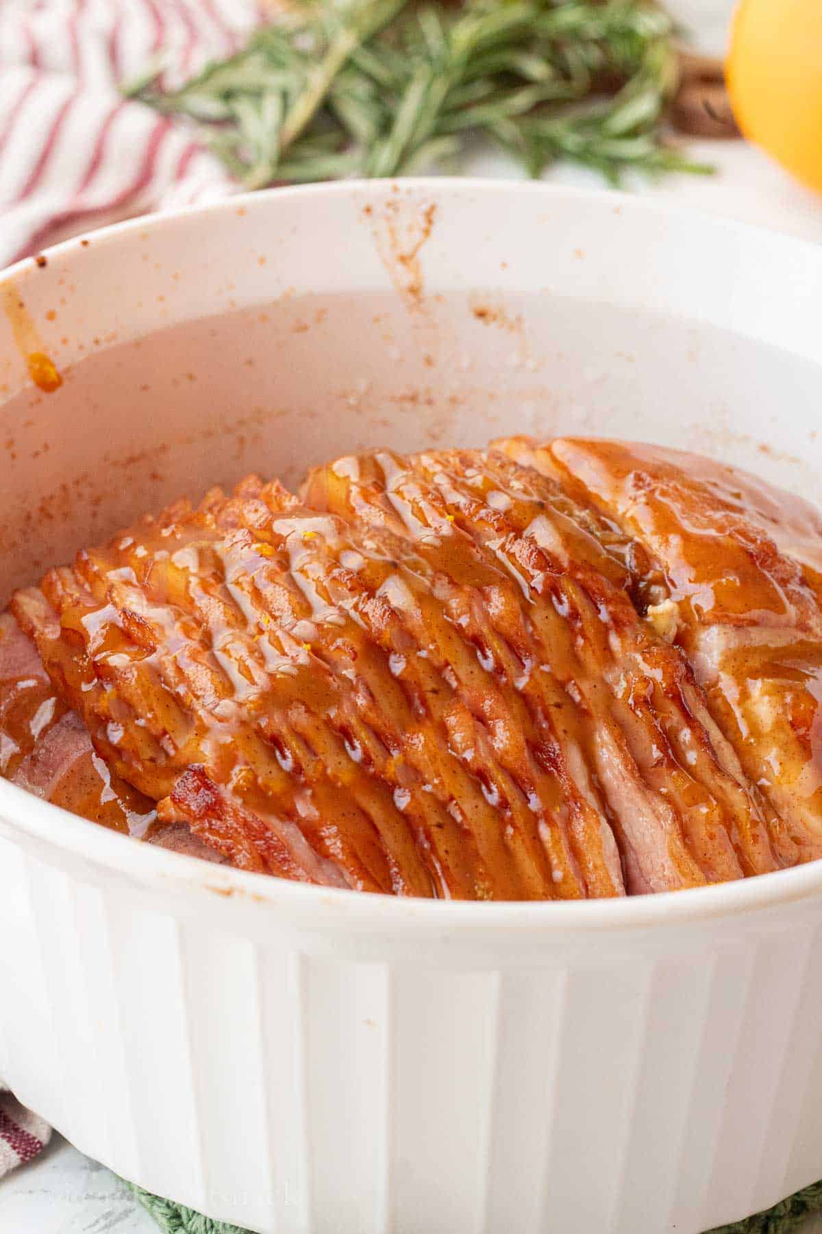 Cooked unglazed ham in white baking dish.