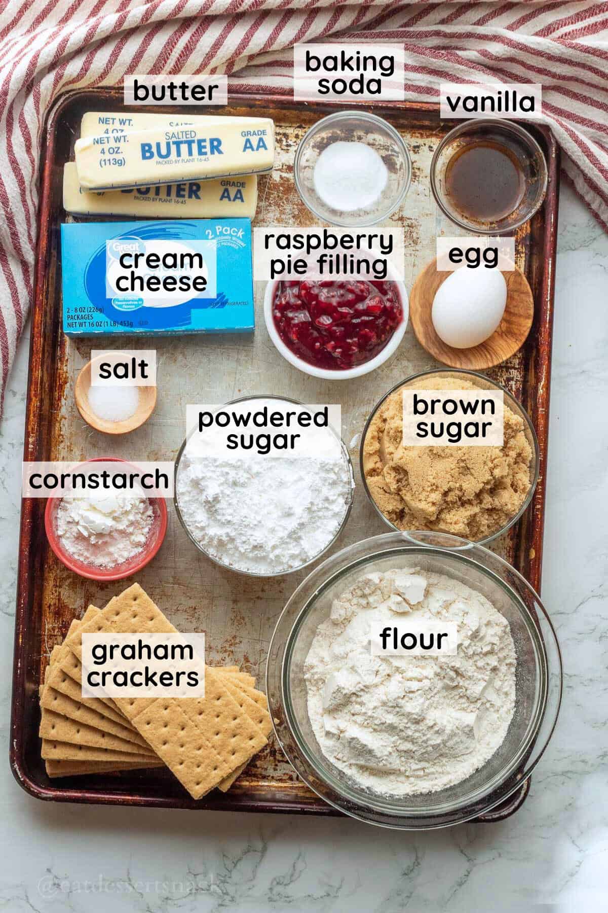 Labeled ingredients for raspberry cheesecake cookies on metal baking pan.