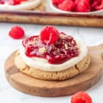 Raspberry pie filling on top of cheesecake cookie on white plate.