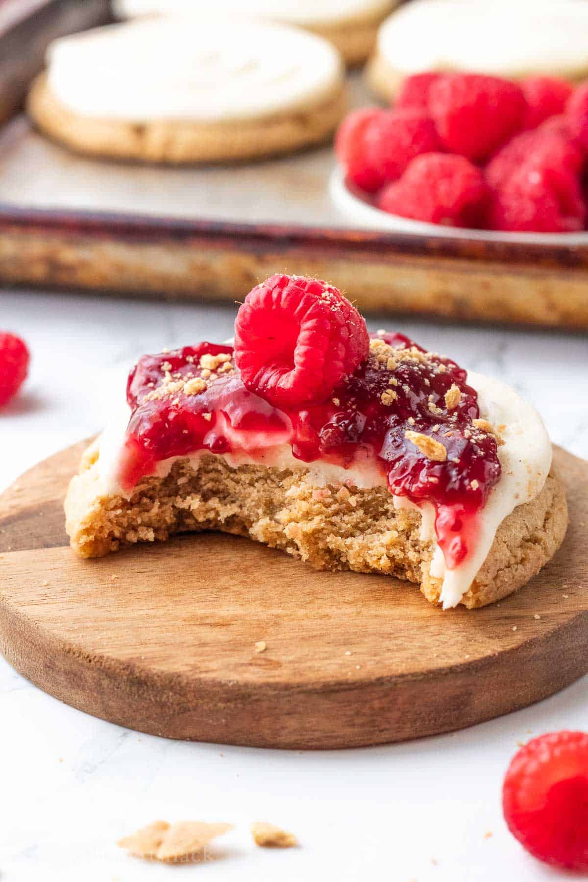 Bite out of raspberry cheesecake cookie on wood cutting board.