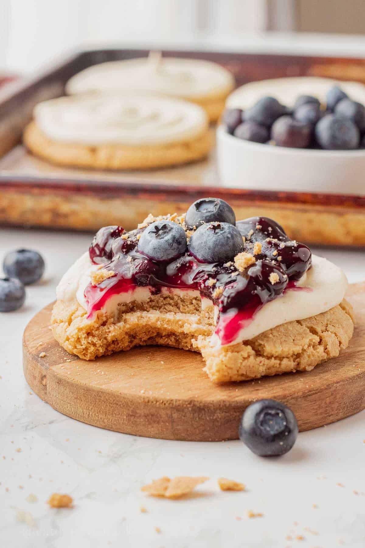 Bite out of blueberry cheesecake cookie on wood cutting board.