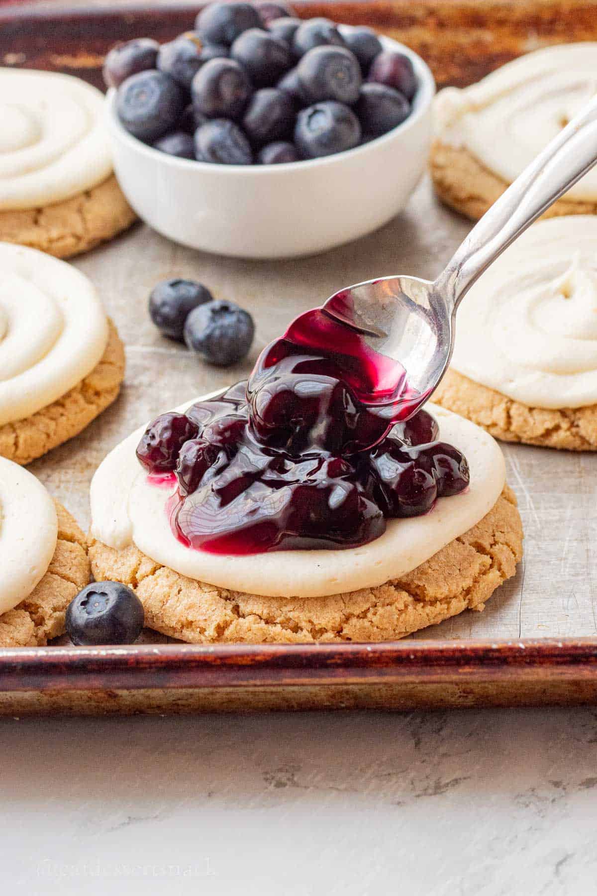 Spooning blueberry pie filling onto cheesecake cookie.