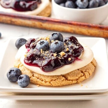 Blueberry pie filling on top of cheesecake cookie on white plate.