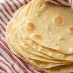 Stack of cooked tortillas in dish towel.