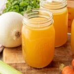 Chicken bone broth in jar on wood cutting board with veggies.