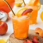 Glass of peach lemonade with slices of lemon and peach and straw.