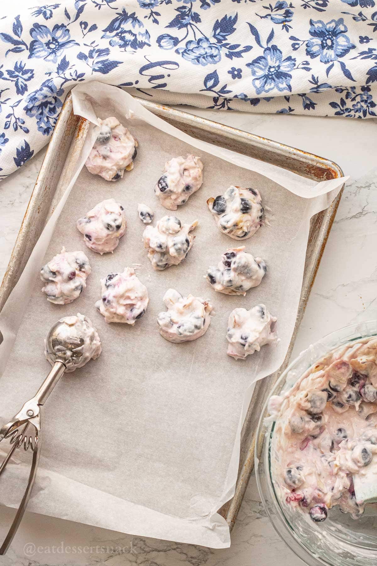Frozen yogurt and blueberry clusters on cookie sheet with metal scoop.