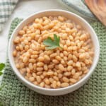 Cooked navy beans in bowl with parsley on top.