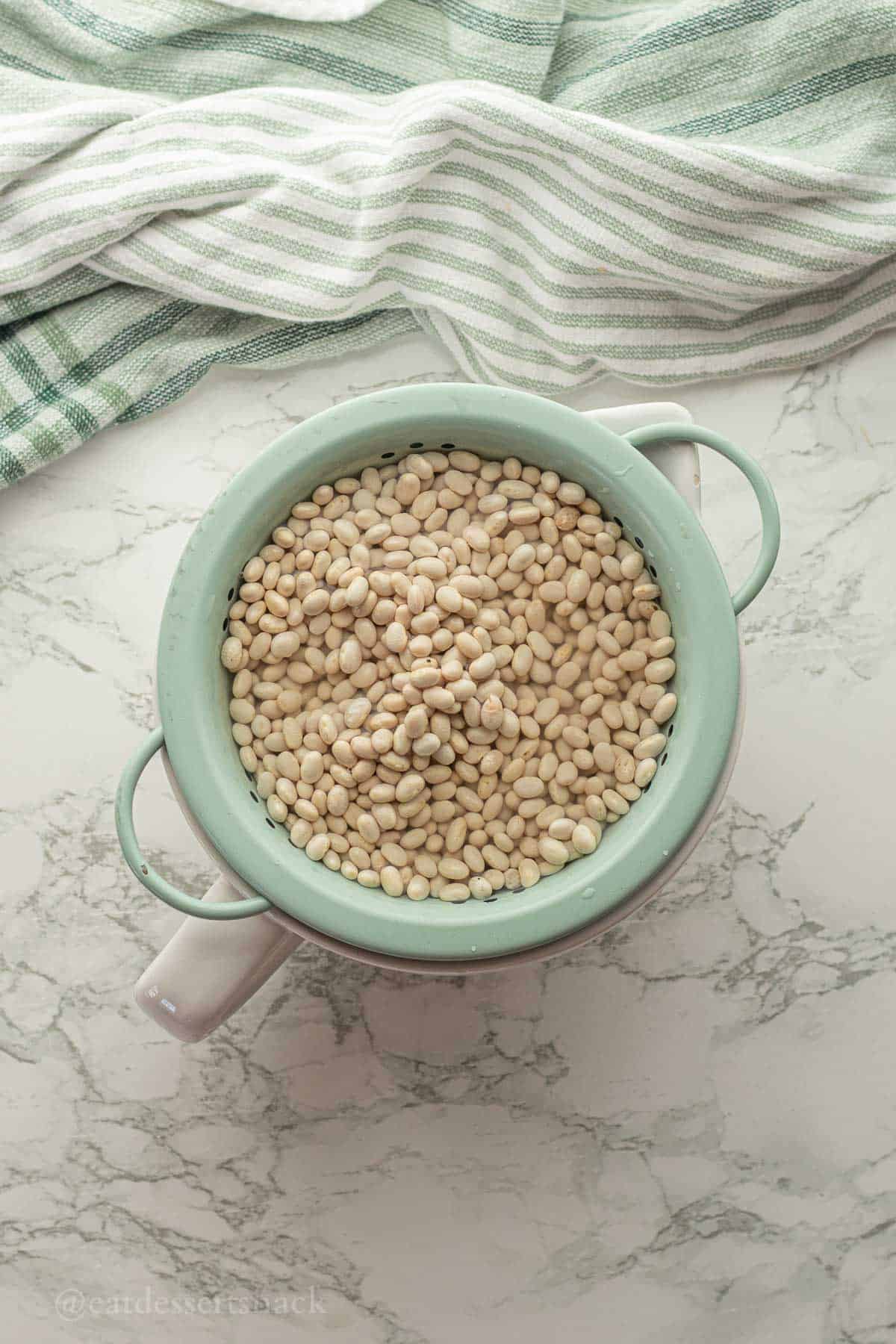 Uncooked navy beans in colander with water.