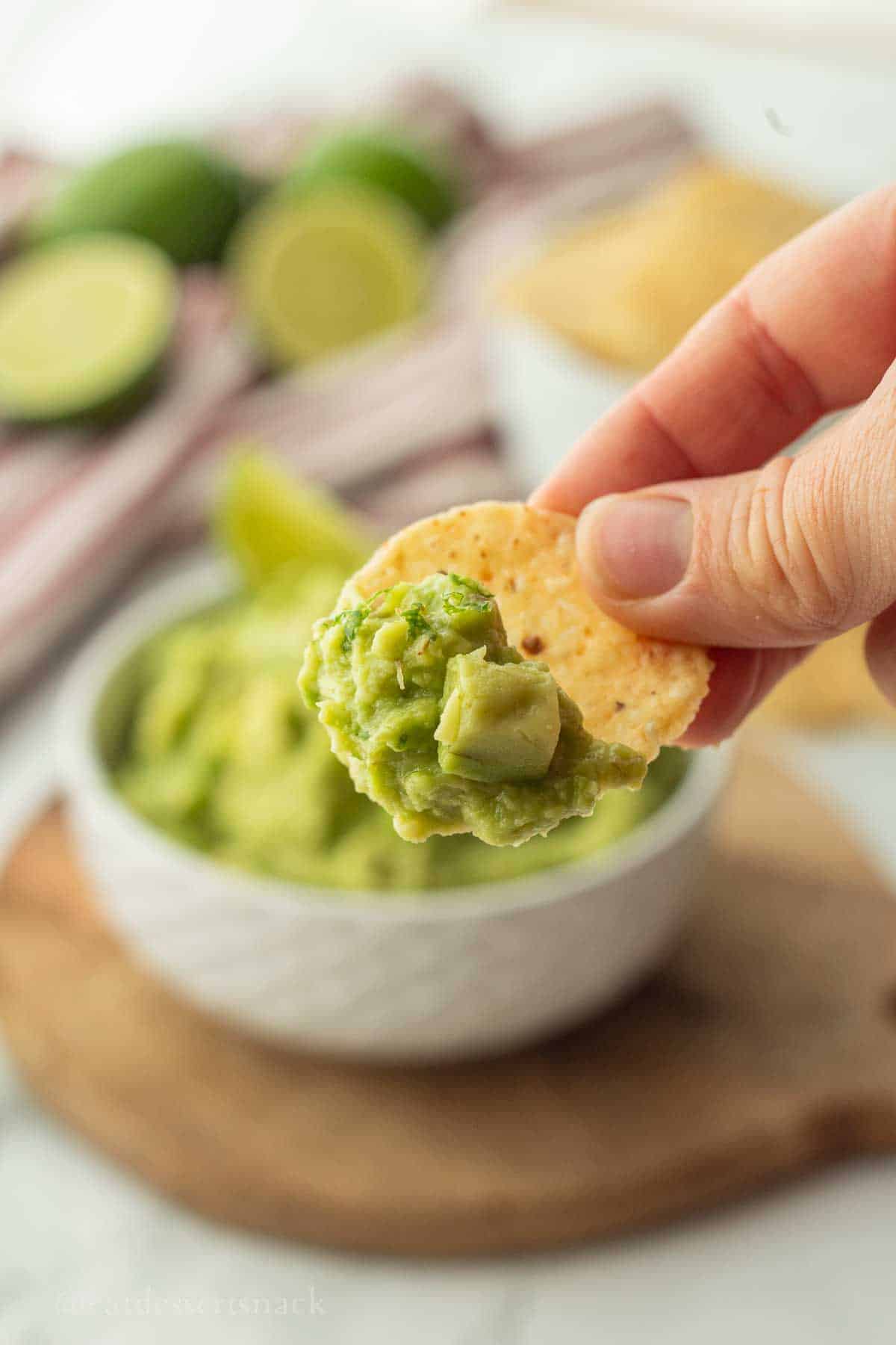 Chip with guacamole above bowl.