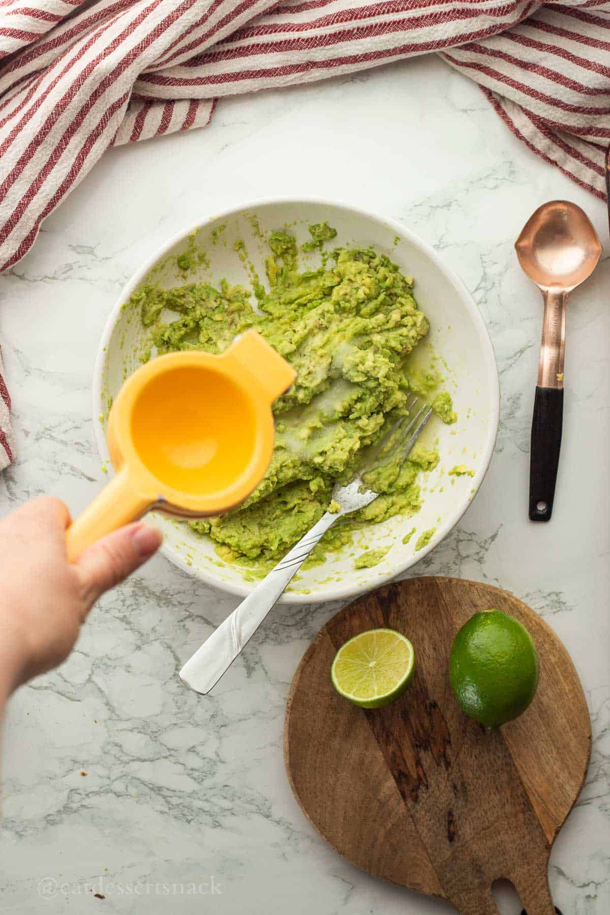 Squeezing lime juice into bowl of mashed avocados.