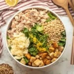 Lemon zest on chicken caesar salad in bowl with wooden spoons.
