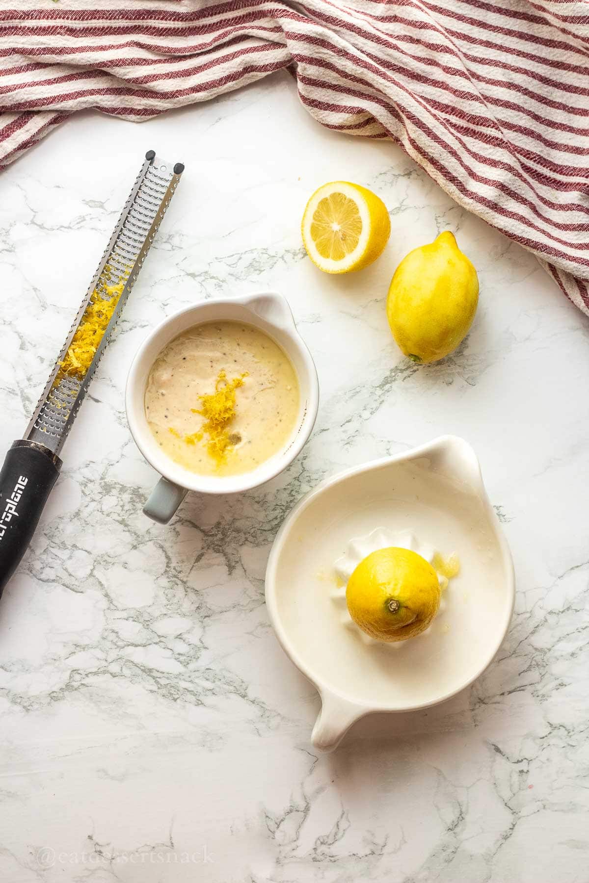 Lemon zest and juice in bowl with zester on marble countertop.