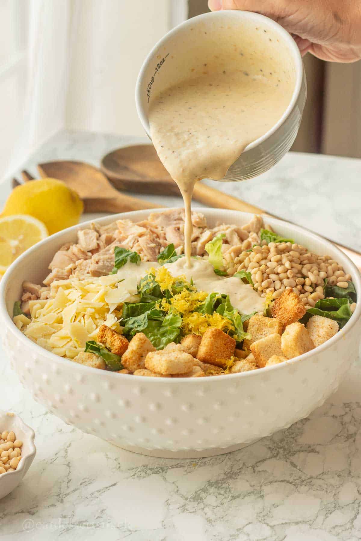 Pouring Caesar dressing onto salad in bowl.