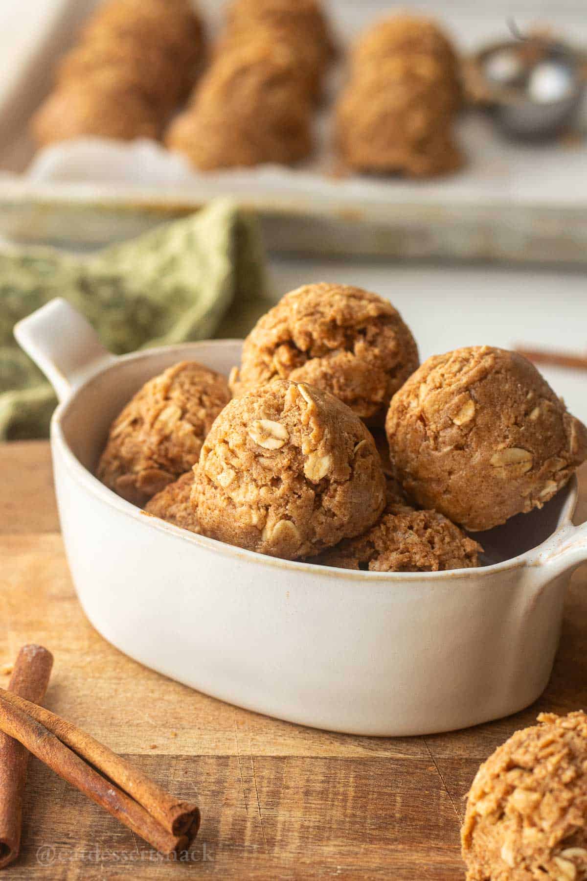 Rolled snickerdoodle protein balls in dish on cutting board with cinnamon sticks.
