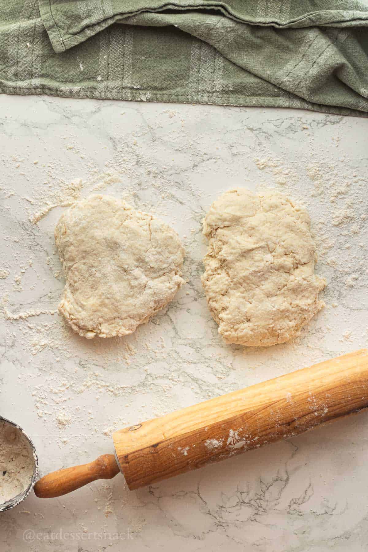2 sections of biscuit dough on marble with flour.