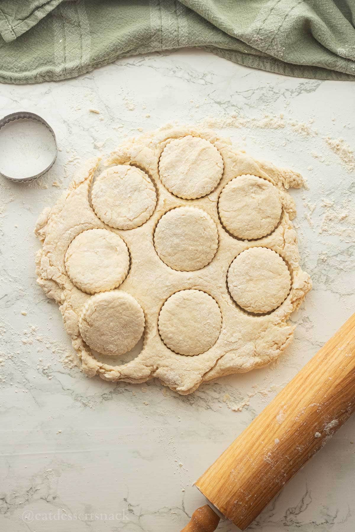 Raw cut biscuits on marble with rolling pin.