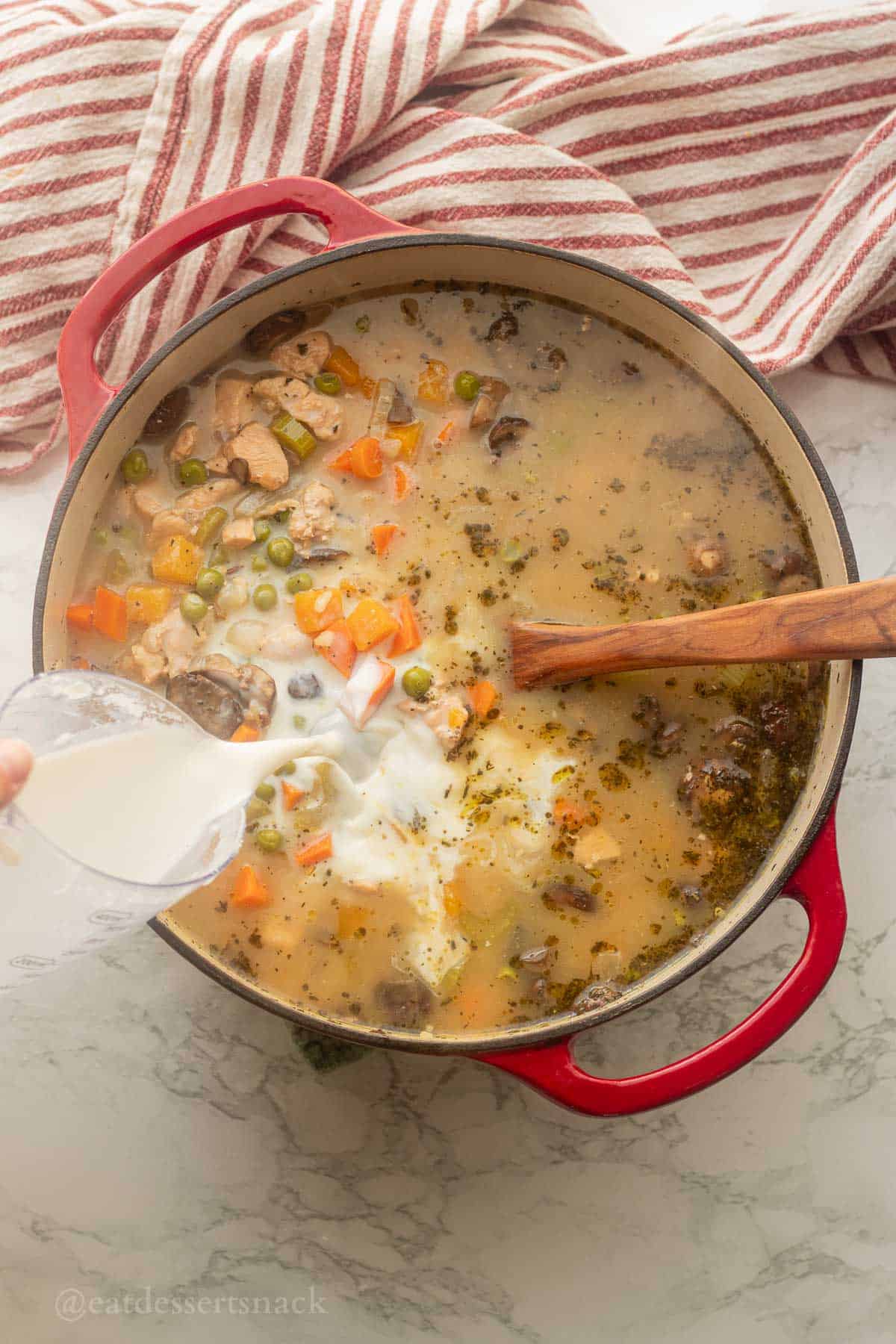Pouring milk into soup pot with spoon.