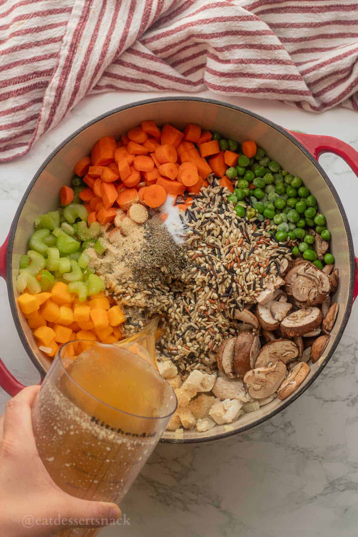 Pouring chicken broth into pot of raw vegetables.