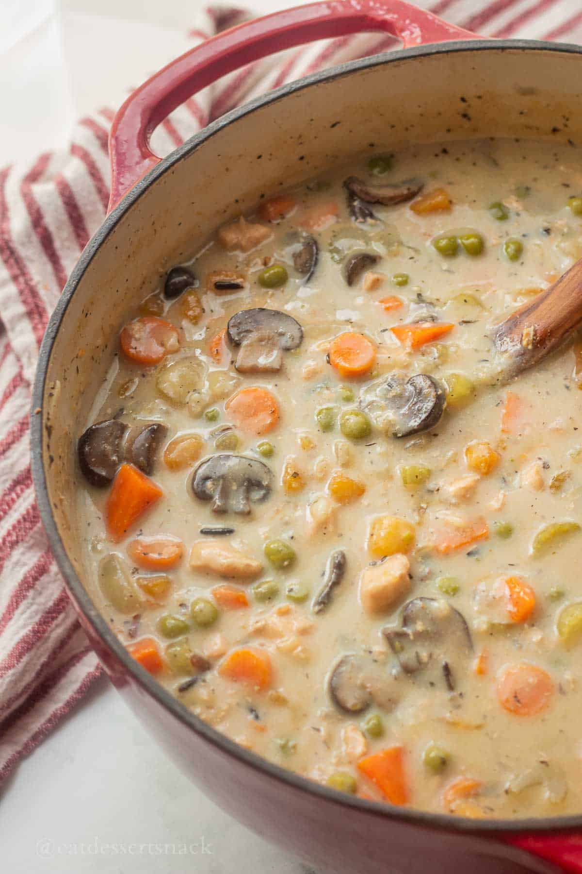 Pot with creamy wild rice soup and wooden spoon in it.