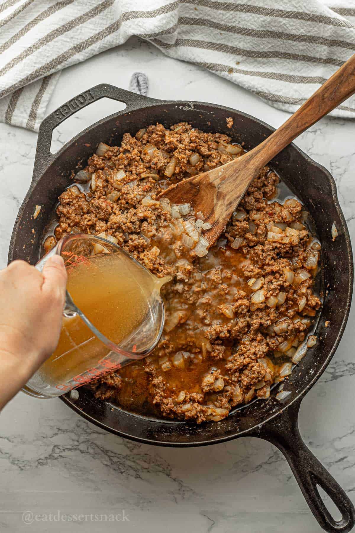 Pouring beef broth into pan of cooked meat and onions.