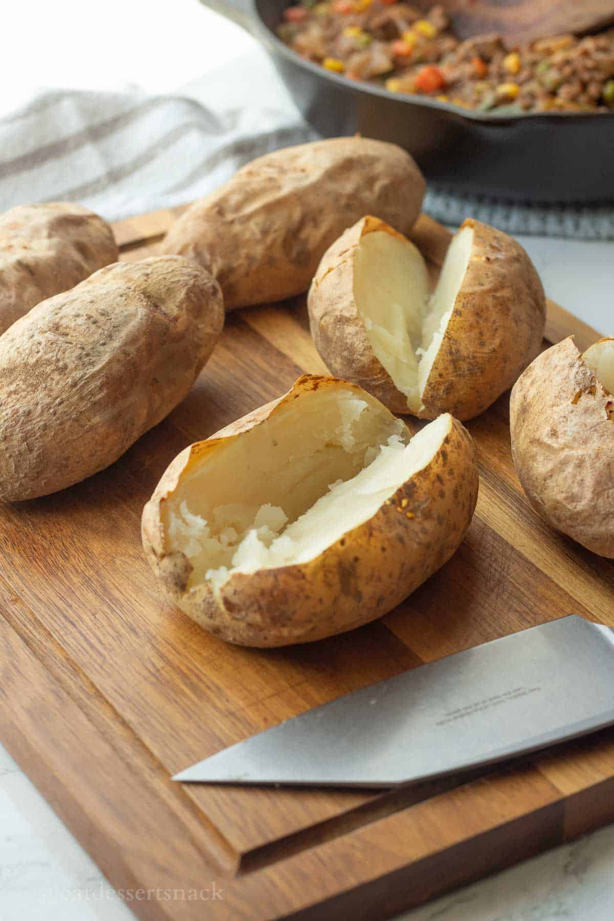 Baked potatoes on cutting board sliced in half.