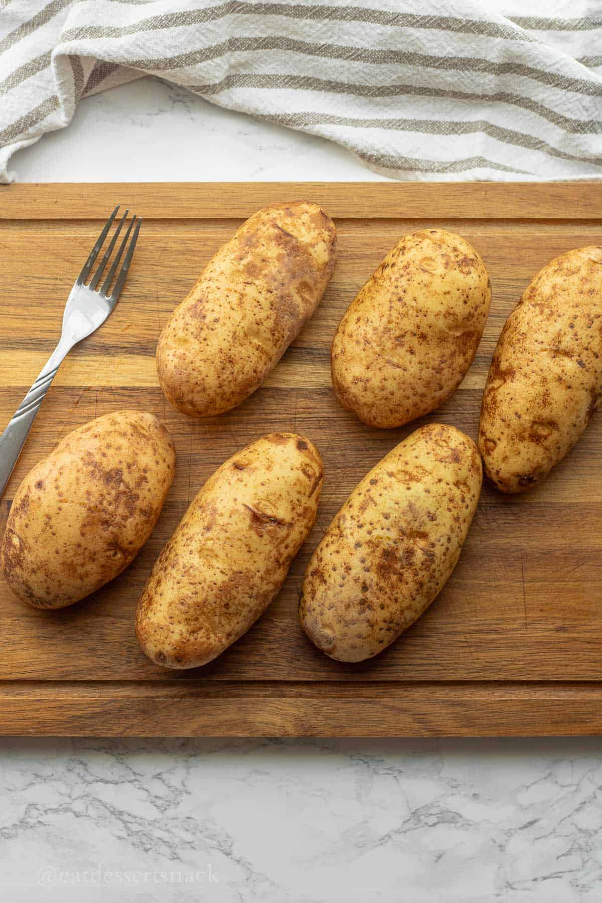 Fork with raw potatoes on cutting board.