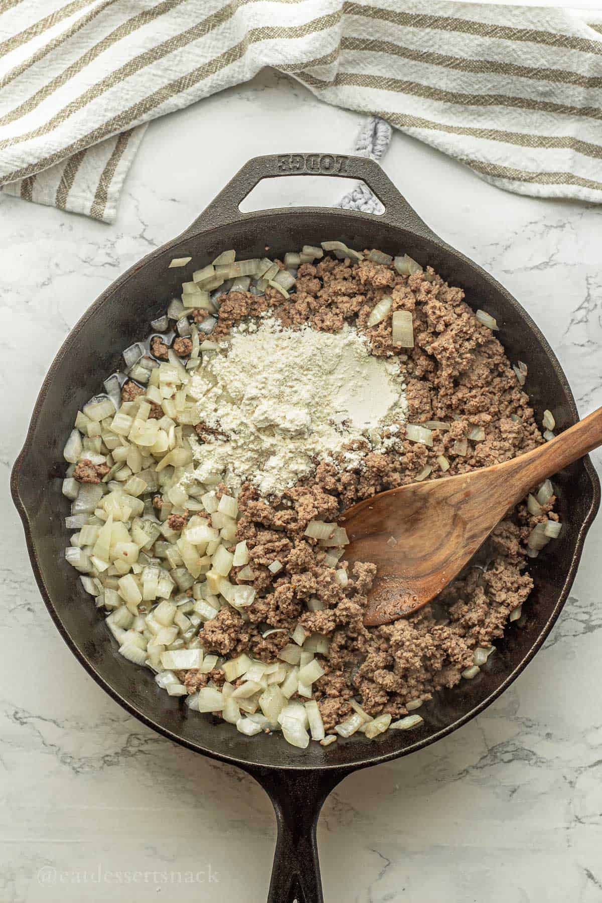 Cooked meat, onions, and flour in pan with spoon.