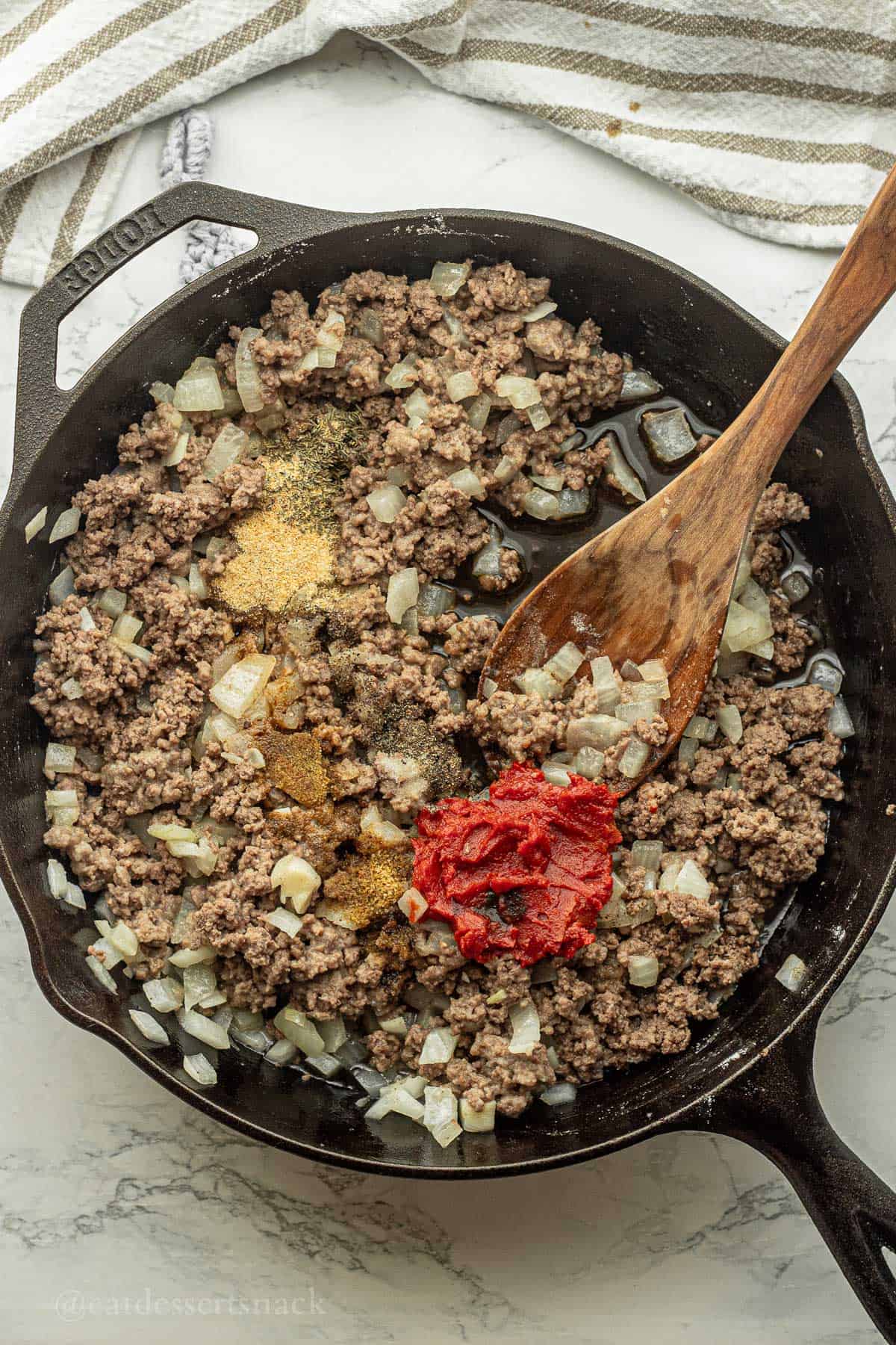 Spices and tomato paste in pan with wooden spoon.