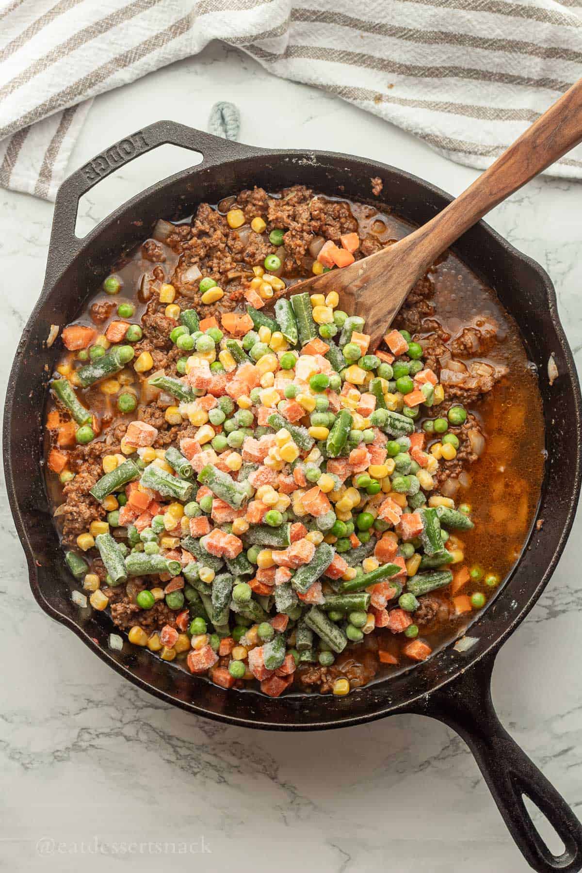 Frozen vegetables in pan with wooden spoon.