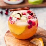 Glass of apple cider punch on wood cutting board with lemon slice.