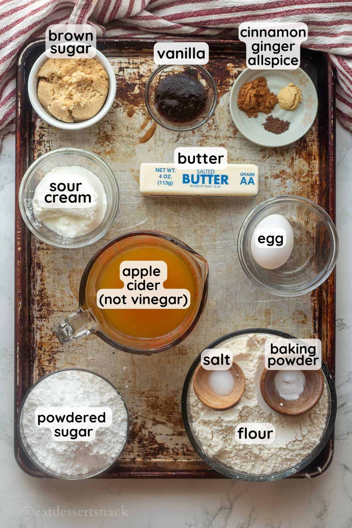 Labeled ingredients for apple cinnamon baked donuts on metal baking tray.