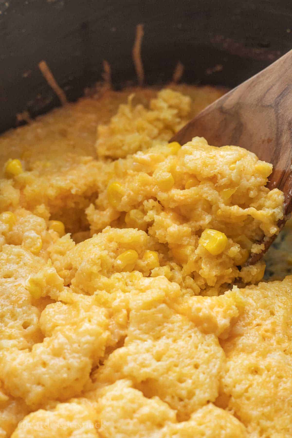 Cooked cornbread pudding in slow cooker on spoon.