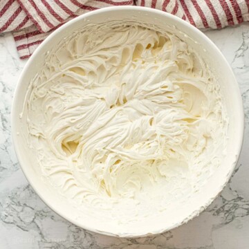 Whipped cream cheese topping in bowl on marble countertop.