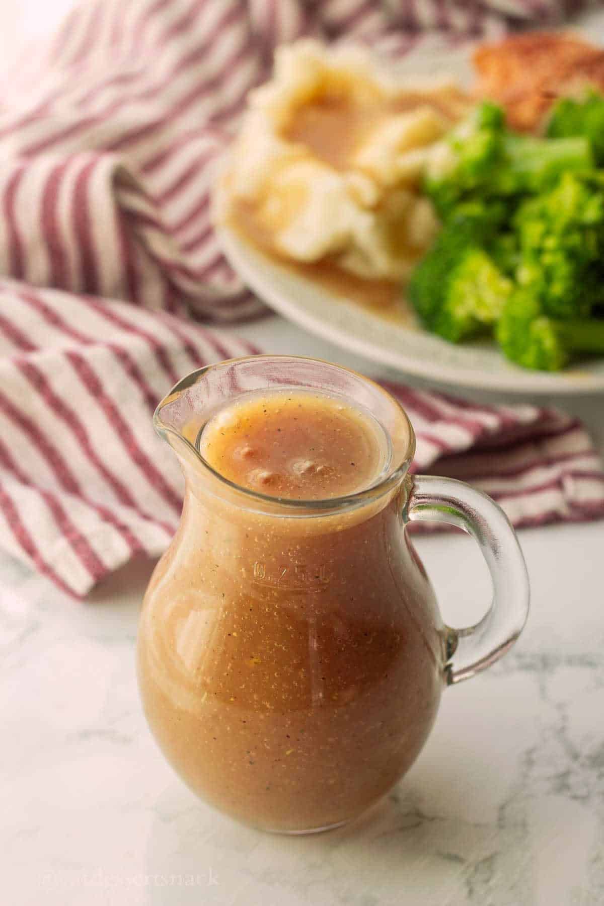 Glass pitcher of gravy on marble.