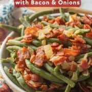 Bowl of cooked green beans with crispy bacon and cooked onions.
