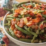 Bowl of cooked green beans with crispy bacon and cooked onions.