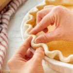 Fingers crimping pie crust in pan.