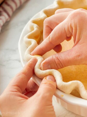 Fingers crimping pie crust in pan.